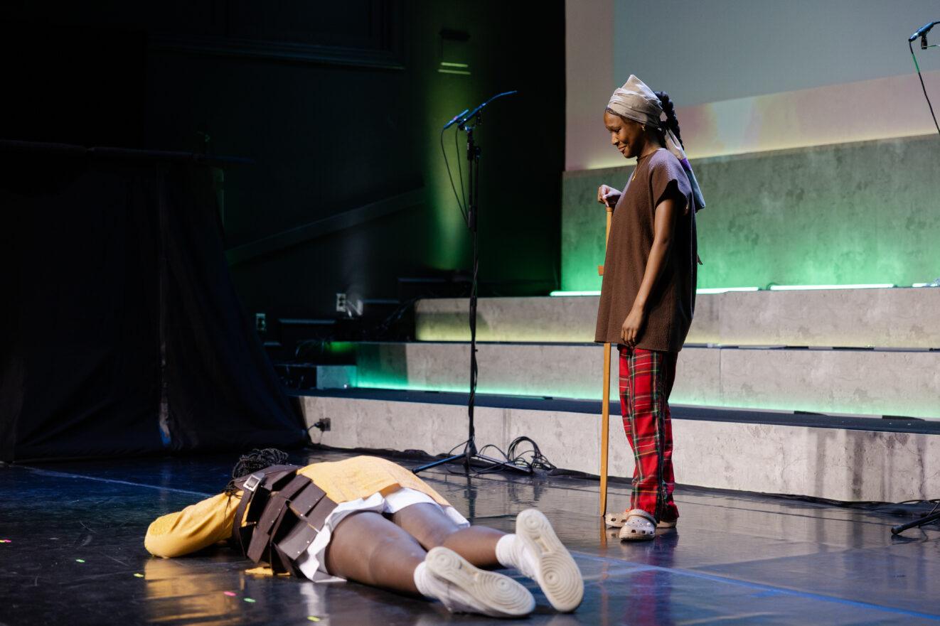 Prielle stands on stage, holding a staff in her hands during a theater production