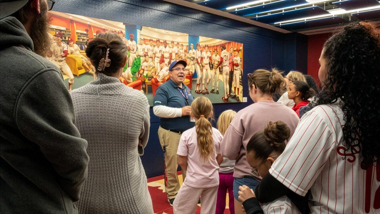 A tour guide speaking to PALCS families in front of a historic Phillies team mural inside Citizens Bank Park.