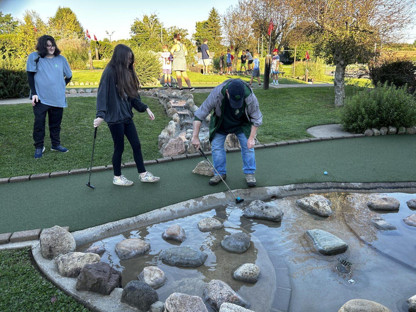 PALCS families playing mini golf together on a sunny outdoor course with water features and greenery.