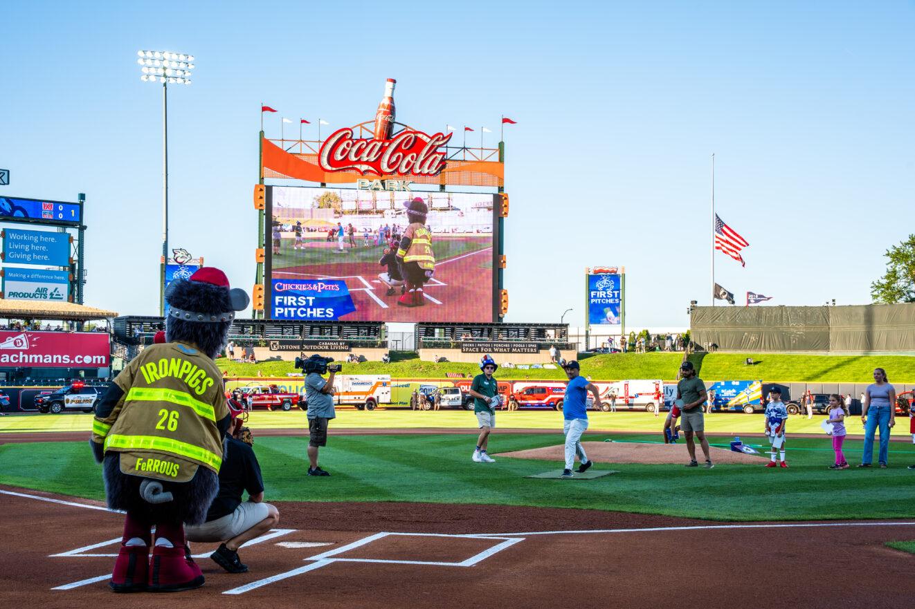 View of the IronPigs baseball field and mascot on the field during PALCS high school principal Michael Logue's ceremonial first pitch under a clear blue sky.