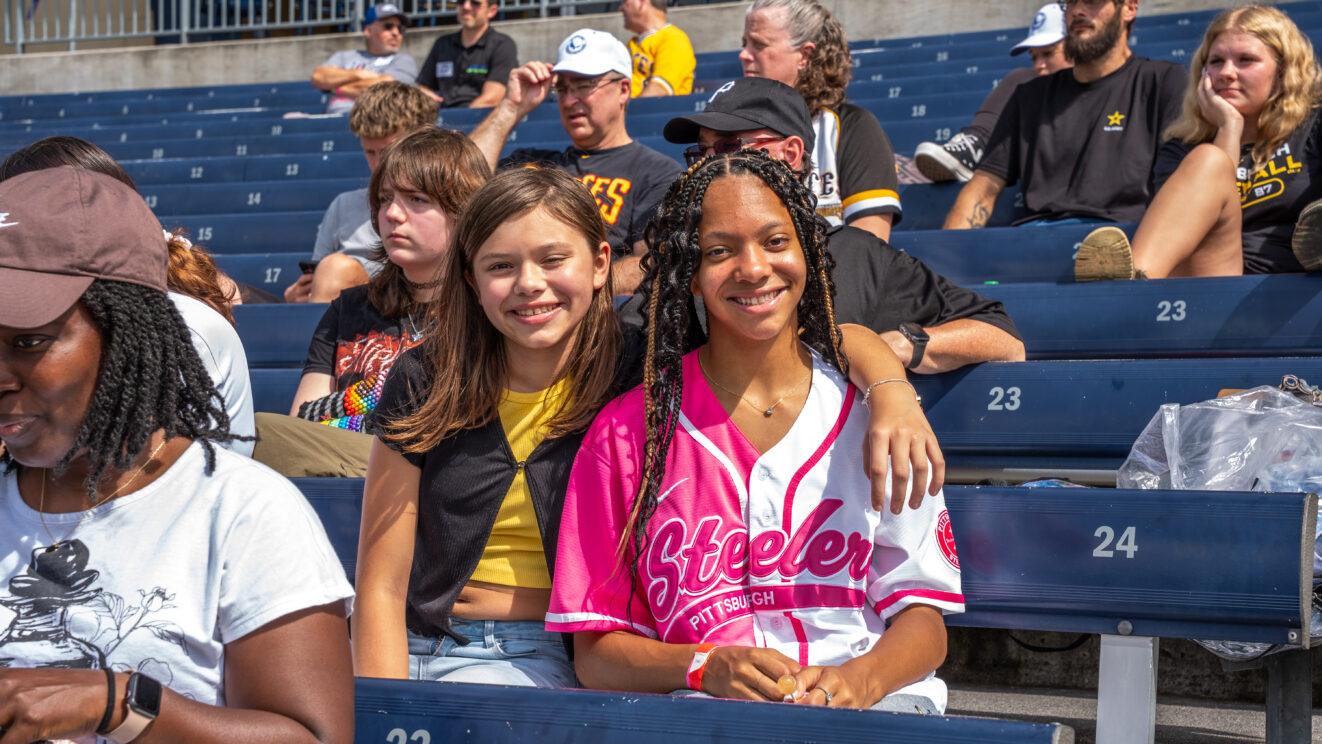 Two girls sitting together in the stadium seating at PNC Park during a Pittsburgh Pirates game.